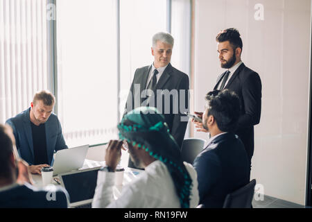 Diverse team of middle-aged multiethnic male investors, leading by senior aged experienced Director, cooperating on developing common investments proj Stock Photo