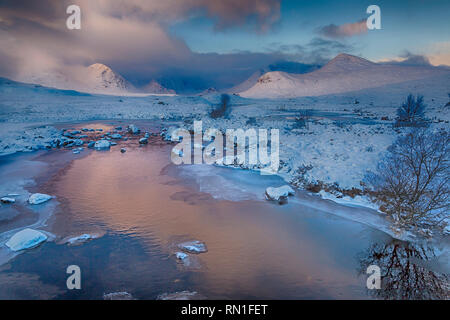 Cold winter morning with partially frozen loch and sunrise reflected in water at Loch Ba, Rannoch Moor, Argyll and Bute, Scotland in January - hdr Stock Photo