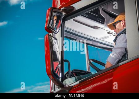 Transportation Industry Theme. Caucasian Truck Driver in His 30s Inside the Red Semi Cabin. Stock Photo