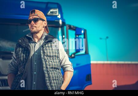 Truck Driving Business Concept. Caucasian Trucker in Front of His Blue Modern Semi. Stock Photo