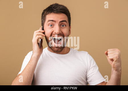 Excited young casual man talking on mobile phone isolated over beige background Stock Photo