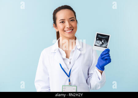 Photo of a young woman doctor posing isolated over blue wall background holding x-ray of baby in hands. Stock Photo