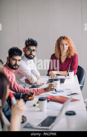 Mixed race diverse group of people in formal wear, sitting in raw at office table attending annual refresher course, led by a red-haired female coach Stock Photo