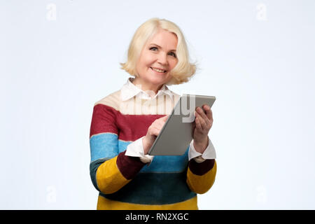 Senior woman using digital tablet surfing web media chatting online, smiling. Stock Photo
