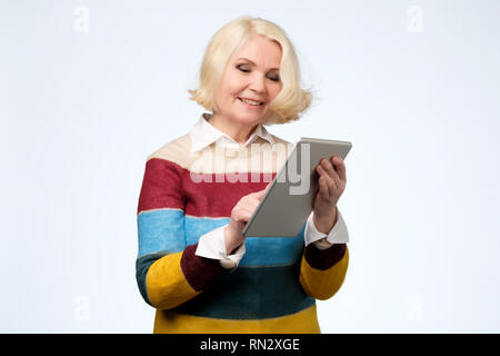 Senior woman using digital tablet surfing web media chatting online, smiling. Stock Photo