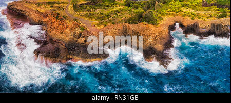 Rugged eroded coasline of Bombo quarry headland on Australian pacific coast with geological basalt hexagonal pinnacle rocks standing up in surfing wav Stock Photo