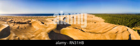 Lifeless eroded sand dunes along long and wide Stockon beach on Pacific coast of Australia in elevated aerial panorama from sea to evergreen woods. Stock Photo