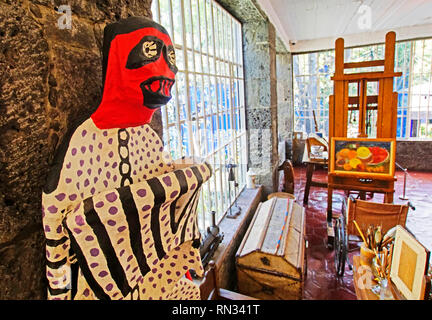 A Frida Kahlo papier-mache folk art sculpture stands next to her easel and wheelchair in her workshop in the Frida Kahlo Museum in Mexico City. Stock Photo