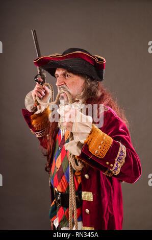 Sea dog, old pirate with musket, holding rope by teeth, studio shot against gray background Stock Photo