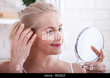 Middle aged woman looking at wrinkles in mirror. Plastic surgery and collagen injections. Makeup. Macro face. Selective focus on the face. Realistic images with their own imperfections. Stock Photo