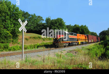 Arkansas train hauls box cars and freight.  Railroad crossing sign sits at highway intersection.  Locomotive is red and black. Stock Photo