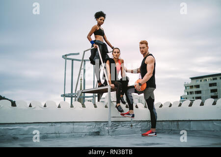Two fitness women with a man relaxing after workout on rooftop standing near the stairs. fitness people standing on terrace after fitness training on Stock Photo