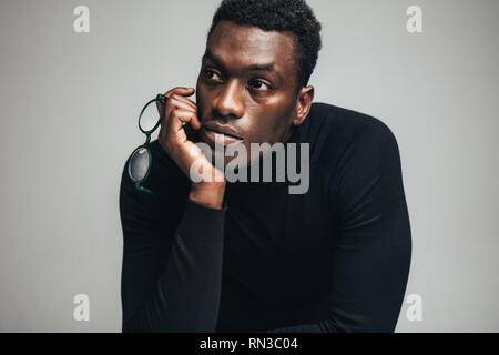 Young african man with eyeglasses looking away on gray background. Thoughtful young african man in black t-shirt. Stock Photo
