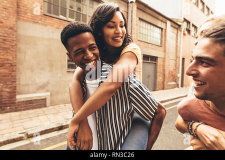Two men giving piggyback ride to their girlfriends outdoors. Multi-ethnic friends having fun outdoors on city street. Stock Photo