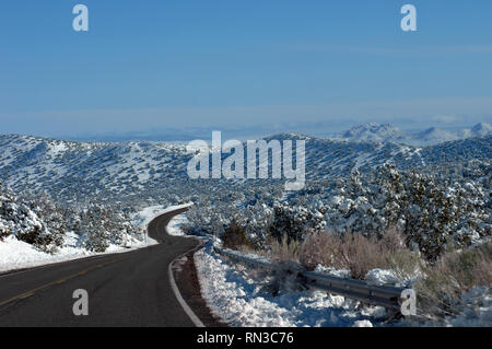 S shaped curving road disappears into the mountaijns of central New Mexico.  Snow covers mountains and trees.  Blue sky. Stock Photo