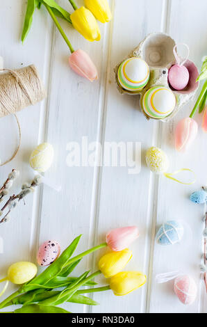 yellow tulips, ginger cookies, willow twigs, decorative eggs in a tray laid out on a white old wooden table, easter holiday background with sweets, fl Stock Photo