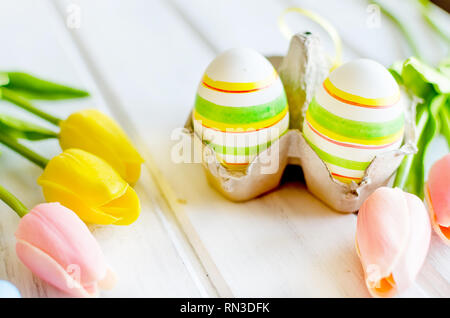 yellow tulips, ginger cookies, willow twigs, decorative eggs in a tray laid out on a white old wooden table, easter holiday background with sweets, fl Stock Photo
