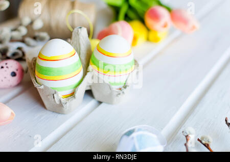 yellow tulips, ginger cookies, willow twigs, decorative eggs in a tray laid out on a white old wooden table, easter holiday background with sweets, fl Stock Photo