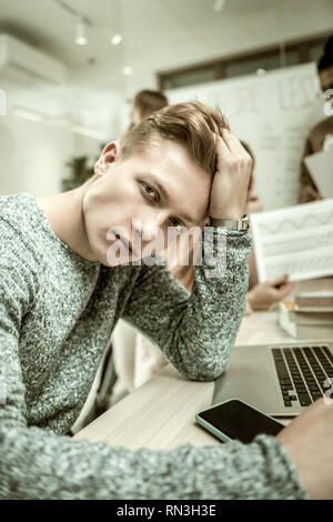 Handsome dark-eyed student wearing grey sweater feeling bored Stock Photo