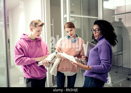 Three students standing near glass doors and revising material Stock Photo