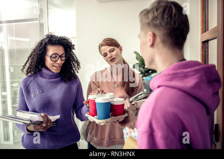 Two students feeling pleased while taking coffee from their friend Stock Photo