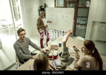 Student wearing grey sweatshirt raising hand asking question Stock Photo