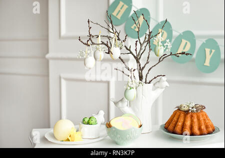 Festive decoration of the Easter table, a vase with a branch and decorations from flowers and eggs, biscuits with rabbit, Easter cake and sweets Stock Photo