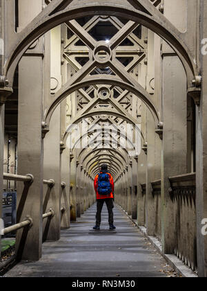 A man stands on the path of repeating iron arches that supports the River Tyne's High Level Bridge between Newcastle and Gateshead. Stock Photo