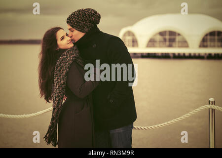 Happy young fashion couple in love kissing outdoor Stylish man and woman wearing classic coats beanie and scarf Stock Photo