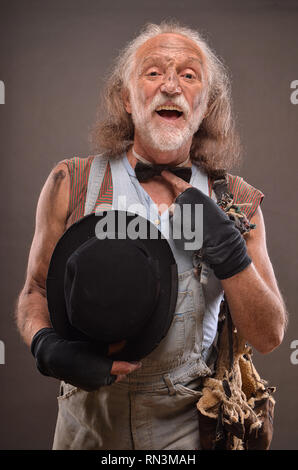 Old homeless but cheerful beggar wearing jeans, black gloves and hat Stock Photo