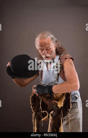 Old homeless tramp wearing jeans, black gloves and hat, carrying shabby lleather bag Stock Photo