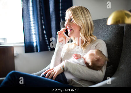 Woman holding her baby son while talking on smart phone Stock Photo
