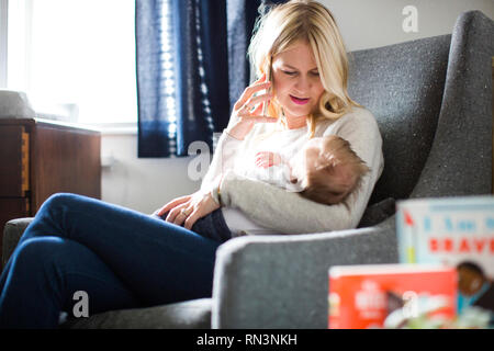 Woman holding her baby son while talking on smart phone Stock Photo