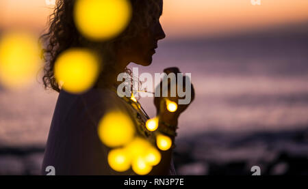 Beautiful woman in the shadow with yello bulb lights - coloured sunset in background - magic and emotional lifestyle concept - dreaming and hope - pra Stock Photo