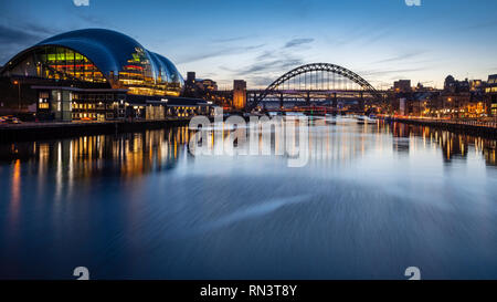 Gateshead, England, UK - February 6, 2019: The Sage Gateshead building and iconic Tyne Bridge are lit at dusk on the River Tyne. Stock Photo