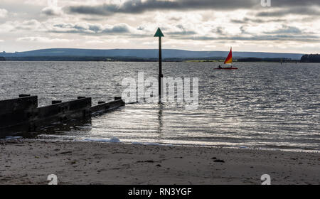 Poole, England, UK - December 26, 2018: A man sails a dinghy at Hamworthy in Poole Harbour, with the Purbeck Hills in the background. Stock Photo