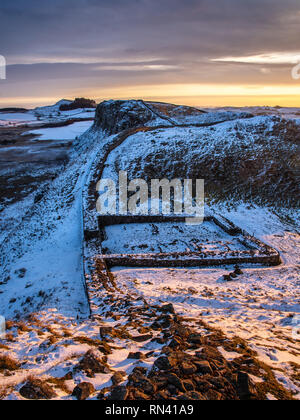 Dawn light illuminates Hadrian's Wall and Milecastle 39 in a dip on the rocky Highshield Crags of Northumberland on a snowy winter day. Stock Photo