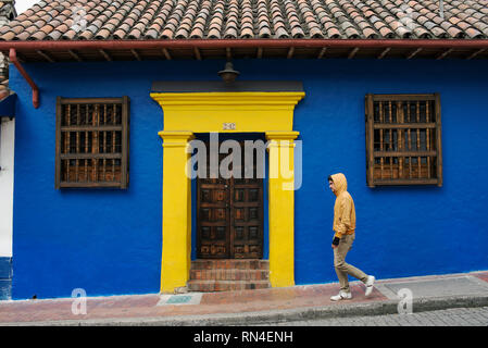 Local resident walking past colonial house wearing casual outfit with matching colours. La Candelaria, the historic town of Bogota, Colombia. Sep 2018 Stock Photo