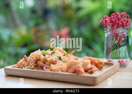 Delicious Thai fried rice with shrimp on wooden table with beauitful vase ,green blurred background Stock Photo