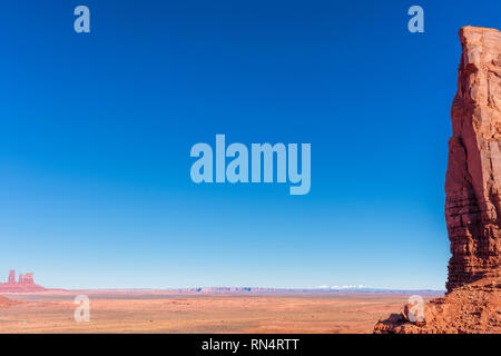 Scenic landscape of dry desert plateau eroded by wind and water with stark red cliff.  Range of snow-capped mountains in the distance under blue sky. Stock Photo