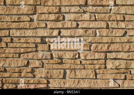 Very rustic looking tan colored stone brick wall with rugged cut stones Stock Photo