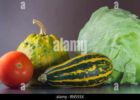 Two green and orange pumpkin on stone desk with tomato and lettuce Stock Photo