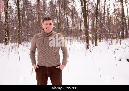 man in a sweater in the winter in the woods. man in the winter forest makes a photo on the phone. Stock Photo