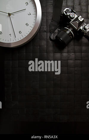 The frenzy of today's times in contrast with the past. A modern design wall clock next to a vintage camera on a black background Stock Photo
