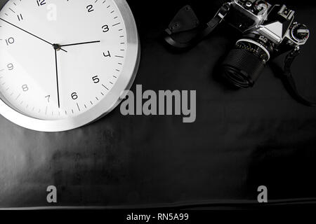 The frenzy of today's times in contrast with the past. A modern design wall clock next to a vintage camera on a black background Stock Photo
