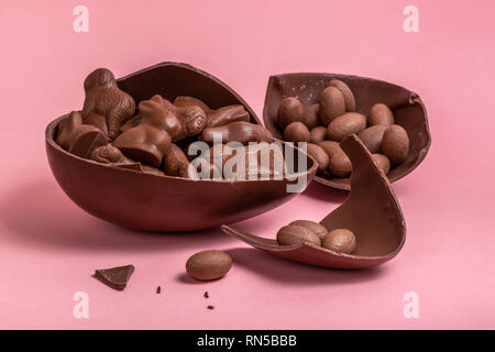 Easter eggs, bunnies and lambs in broken chocolate Easter egg over pink background Stock Photo