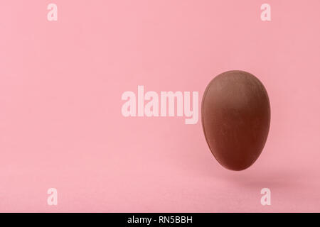 funny creative concept of flying chocolate egg over pink background, copy space Stock Photo