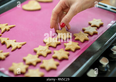 Female hand placing star shaped cookie dough on a pink baking mat. Stock Photo