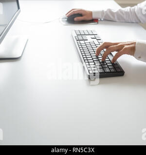Computer programmer working using his office computer, keyboard and mouse as he develops a program. Stock Photo