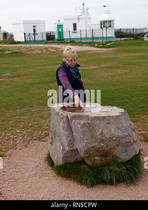 Woman pointing at compass plaque on rock at berry head with the lighthouse behind, Brixham, Devon, UK Stock Photo